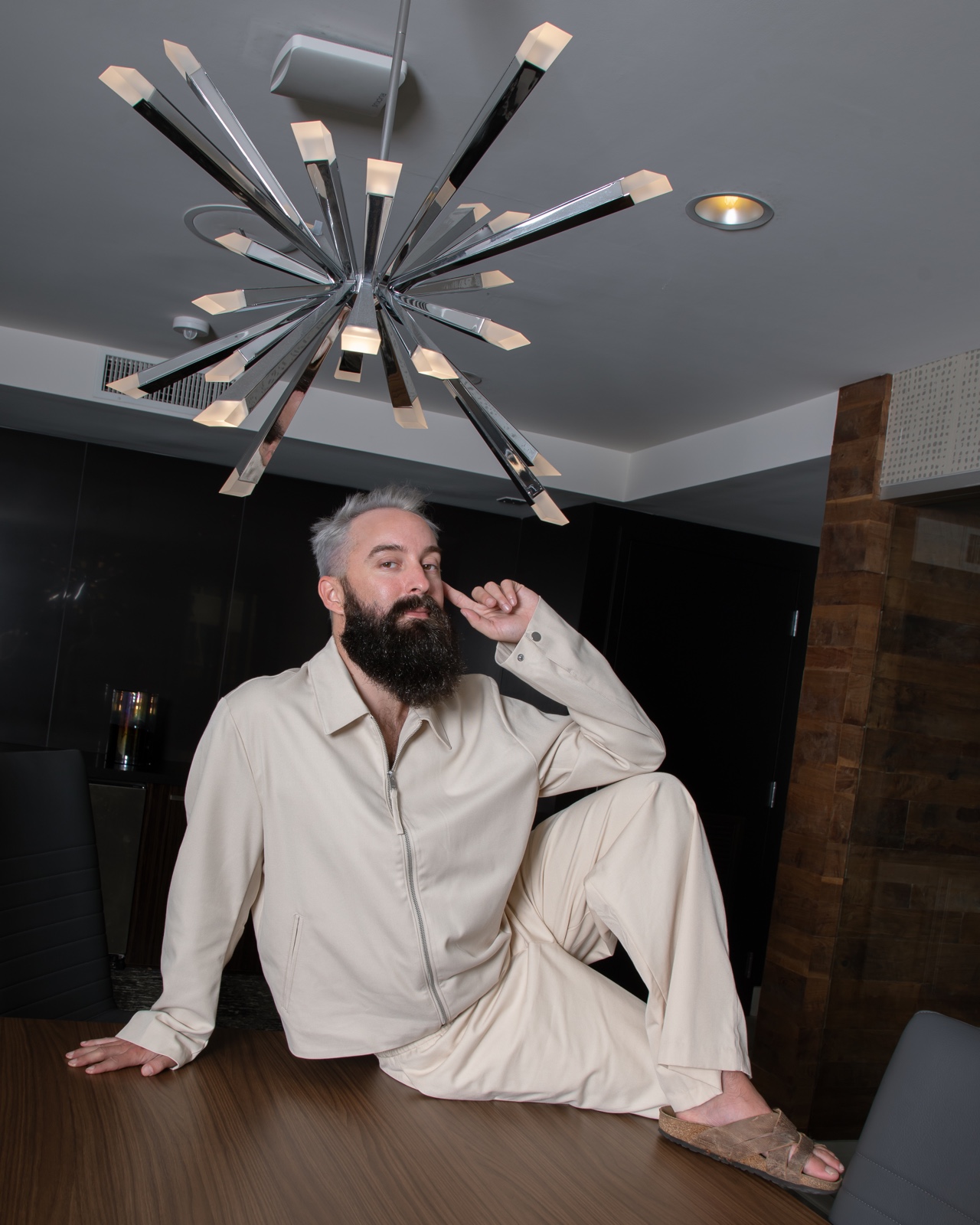 Dylan in a cream outfit, seated on a table beneath a sculptural light